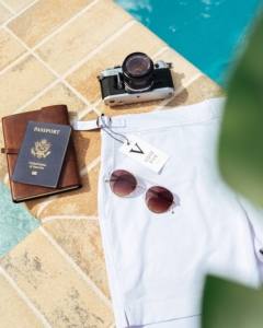 By the pool, with sunglasses, a passport and a camera on a tiled pool surround
